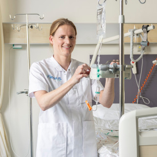 Een verpleegkundige in uniform controleert een infuus in een ziekenhuiskamer.